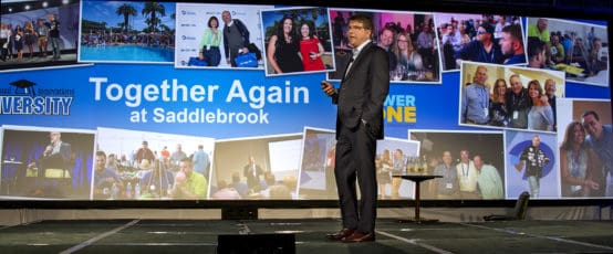 Suit-clad man on stage, screen shows Together Again at Saddlebrook with event photos; conference setting.